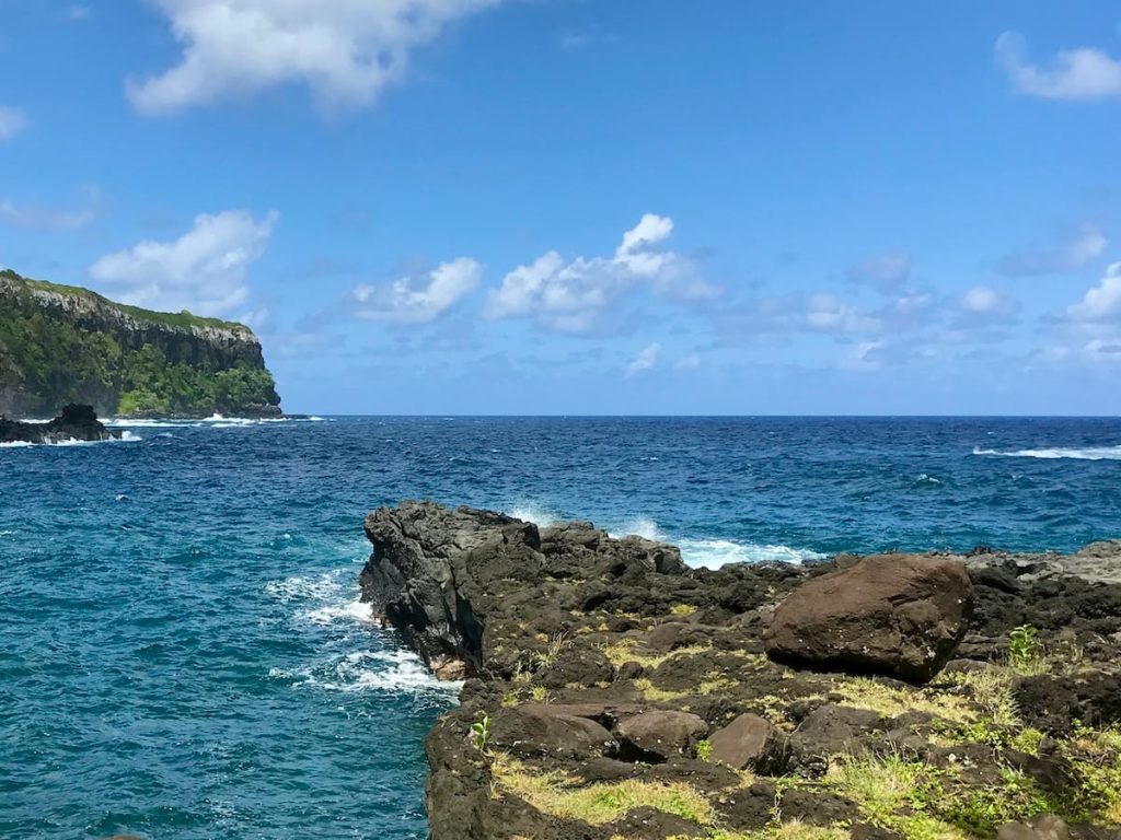A rocky coastline with a cliff in the distance under a blue sky with scattered clouds.