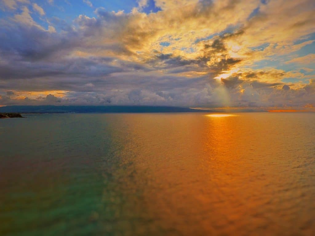 A vibrant sunset over the ocean, with the sky painted in shades of blue, orange, and yellow, reflecting on the calm water below.